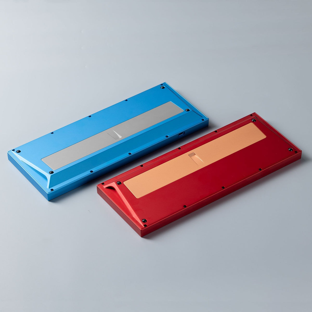 Zwei KBDFans Chamber TKL Gehäuse von unten, blau und rot, mit sichtbarem silberfarbenem und kupferfarbenem Gewicht