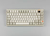 KKB Classic Beige Keycaps ISO-DE in beige and grey on a beige keyboard, top view with brass badge and orange dial