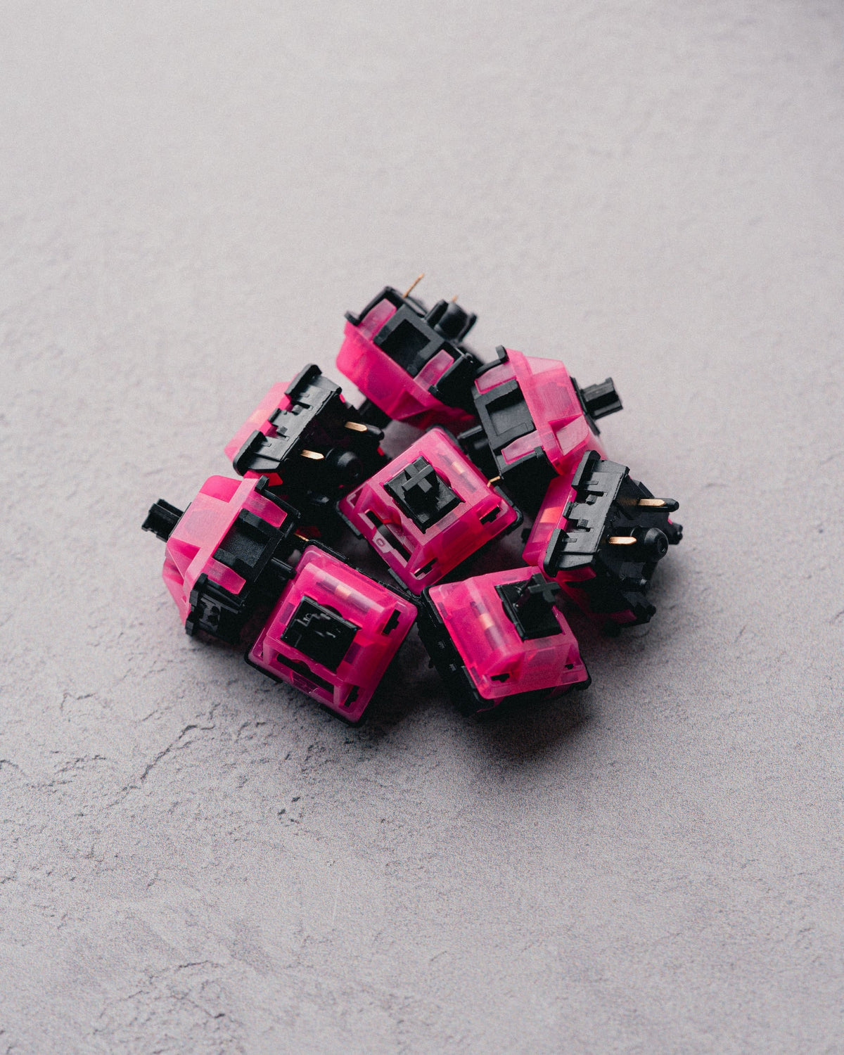 F-ROW Hollow Tips Switches mit pinkem, transparentem Gehäuse und schwarzem Stem, auf einem Haufen auf grauem Stein