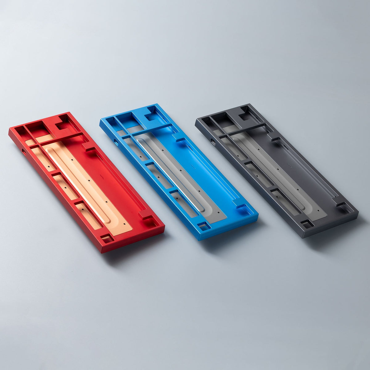 Drei leere KBDFans Chamber TKL Gehäuse in Rot, Blau und Dunkelgrau nebeneinander auf hellgrauem Untergrund